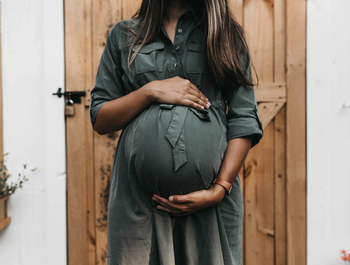 A woman holding her belly in front of a wooden door.